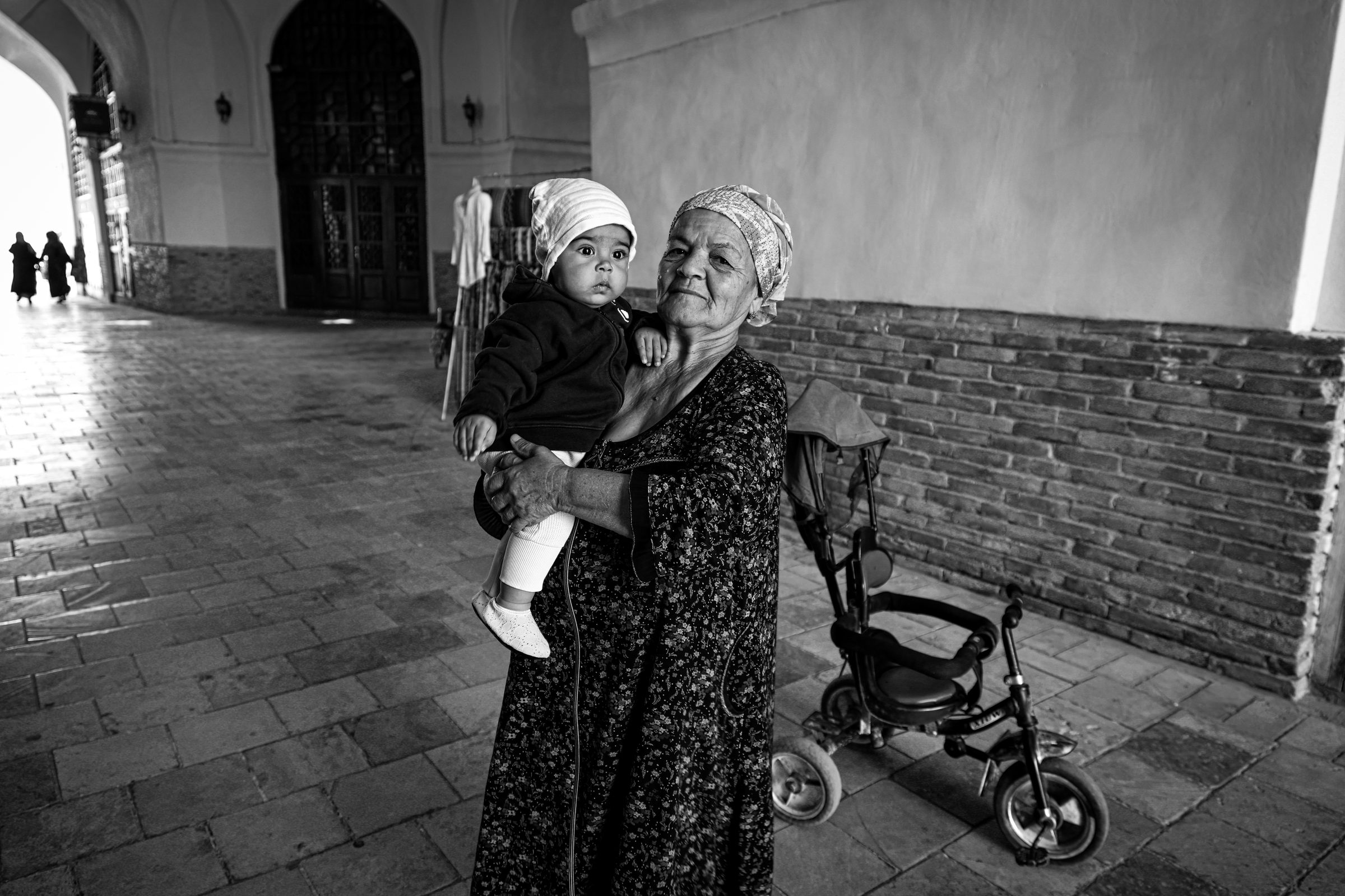 A grandmother holding a child beneath an archway, Uzbekistan