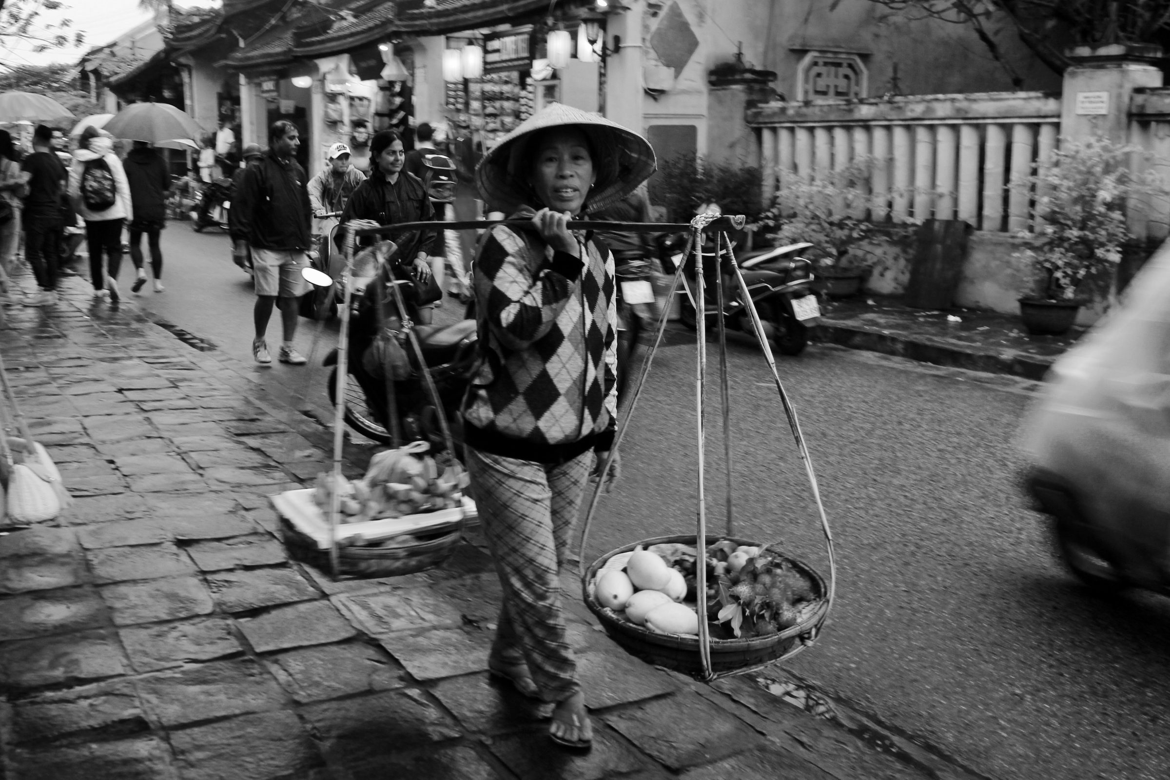 A fruit vendor carrying baskets on a shoulder pole, Hoi An